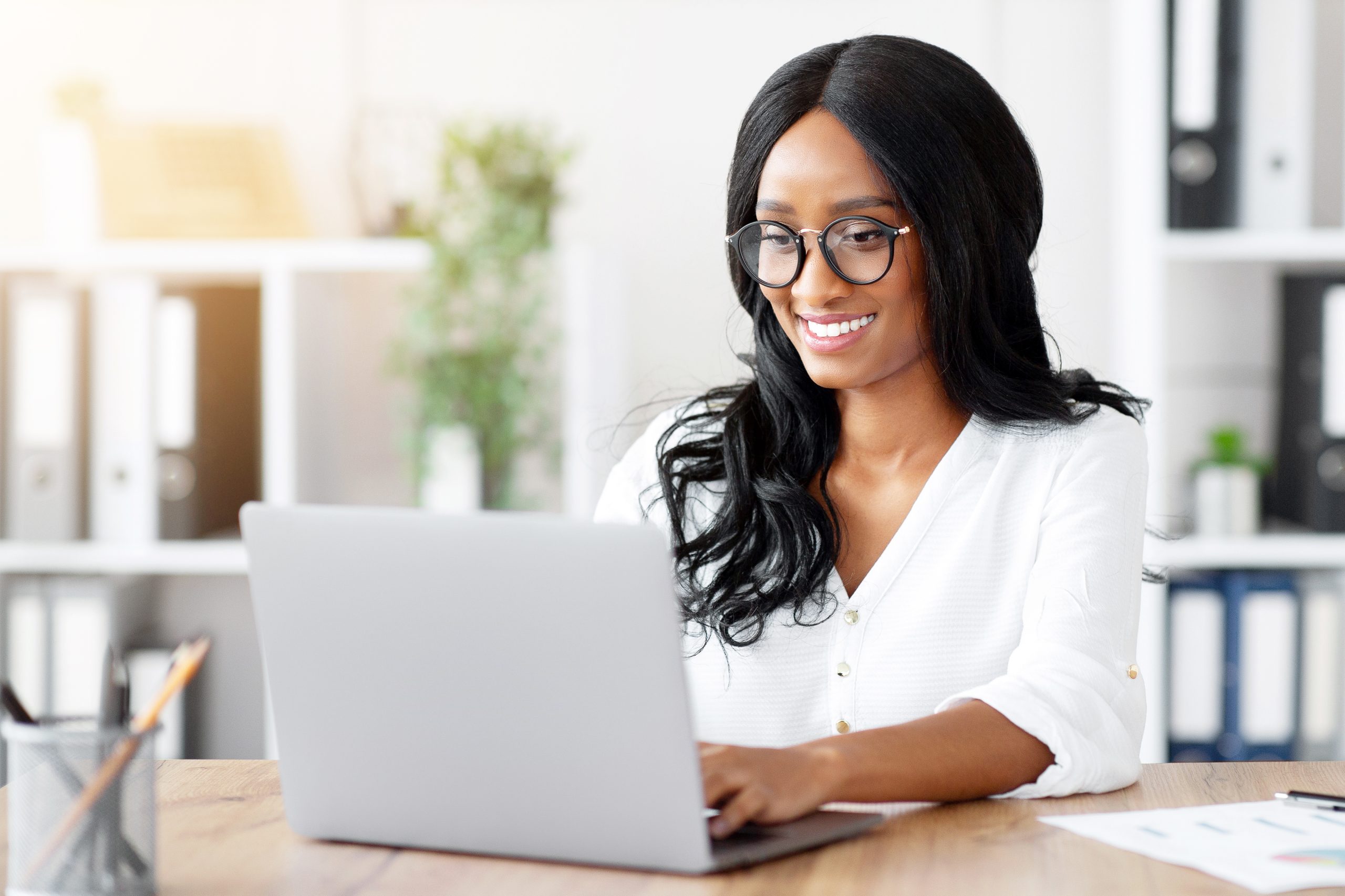 Smiling Black woman attending an online class on her laptop from a bright home office.