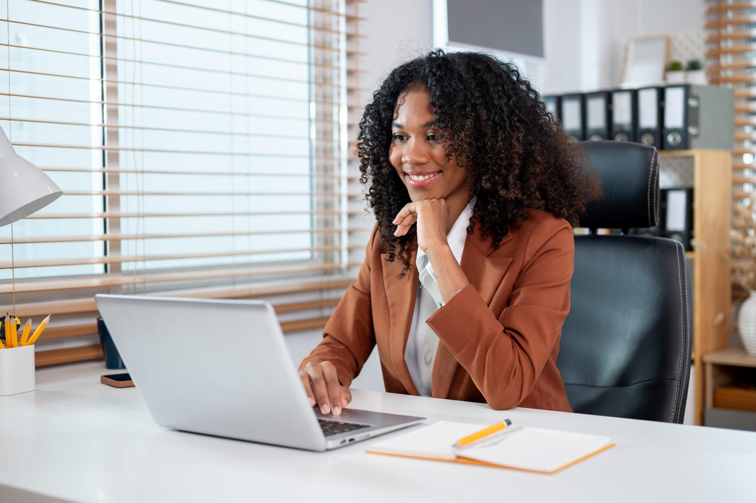 Smiling professional woman working on a laptop in a modern office, representing success in a BA in Public Administration program.