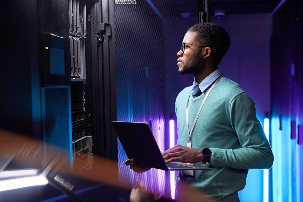 Cloud specialist using a laptop in a server room.