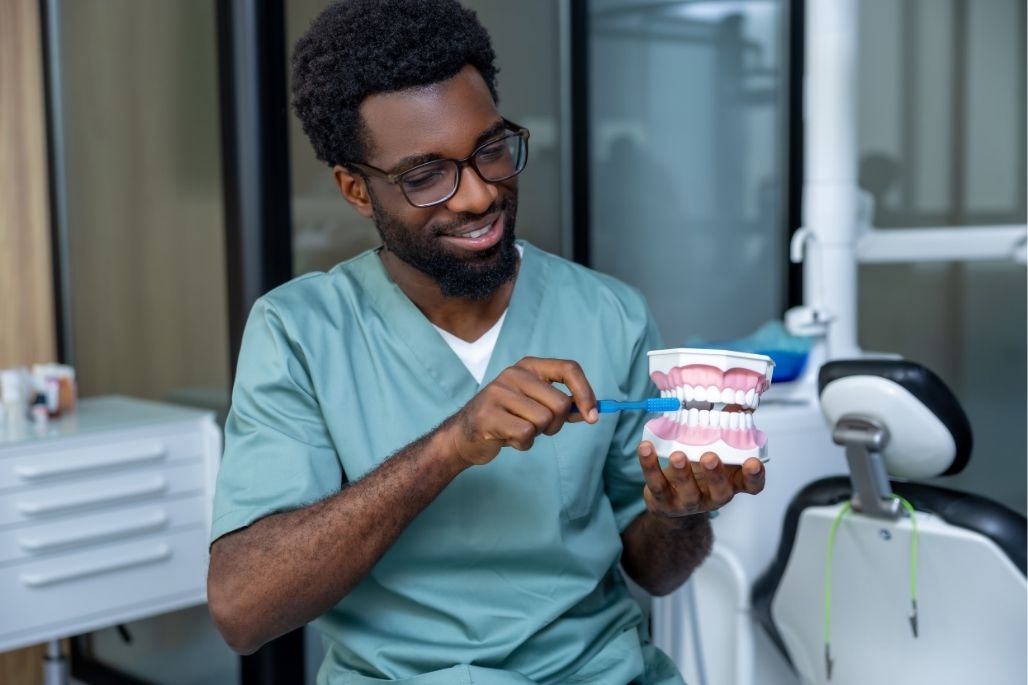 Dental assistant demonstrating tooth brushing on a dental model in a clinic.