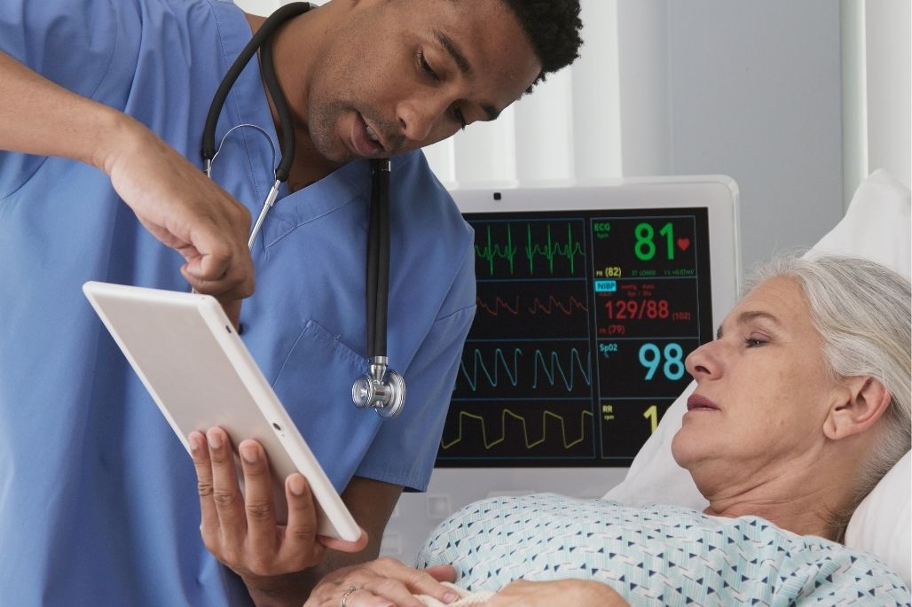 EKG technician reviewing heart rhythms on a monitor in a hospital room.