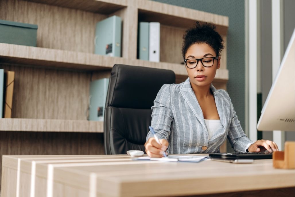 Medical office administrator reviewing patient files at a desk in a clinic.