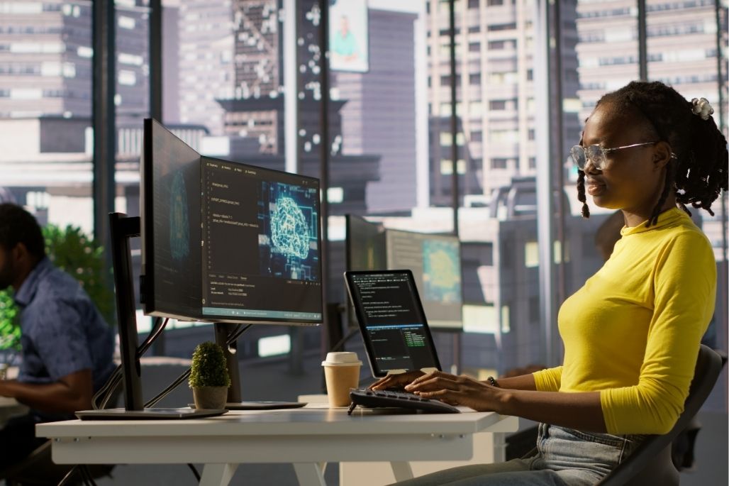 Cybersecurity analyst reviewing code on dual monitors in a lab.