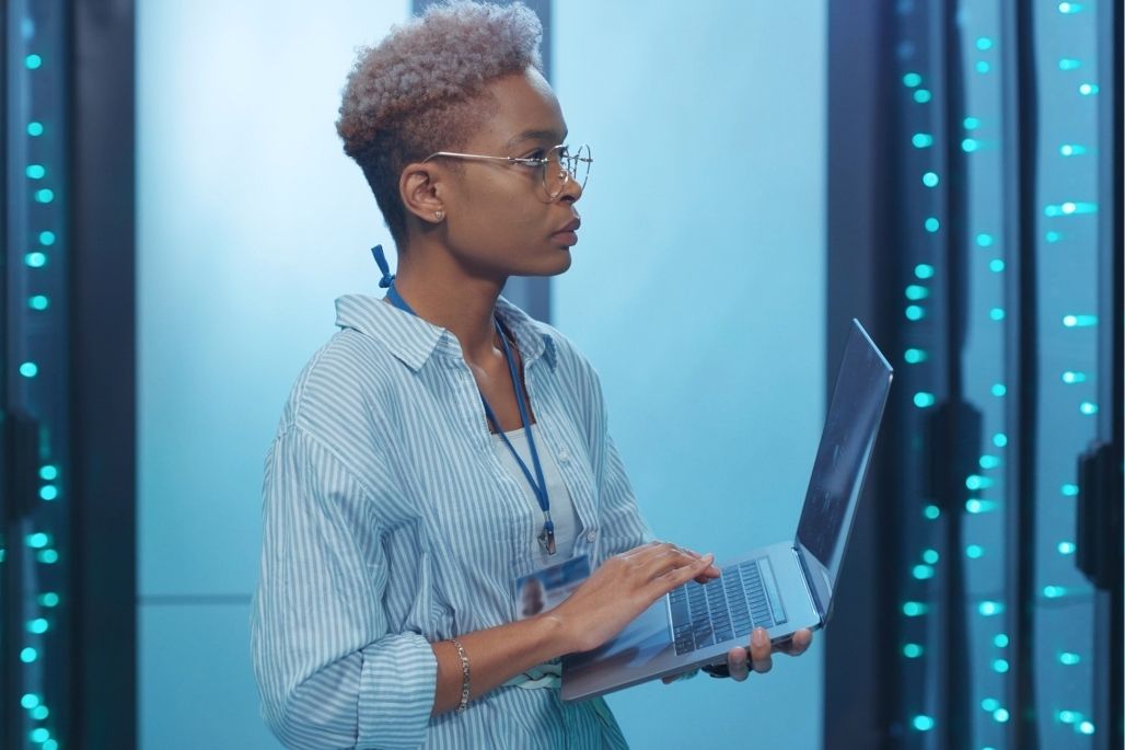 Information Systems Security Professional working with laptop in a secure server room.