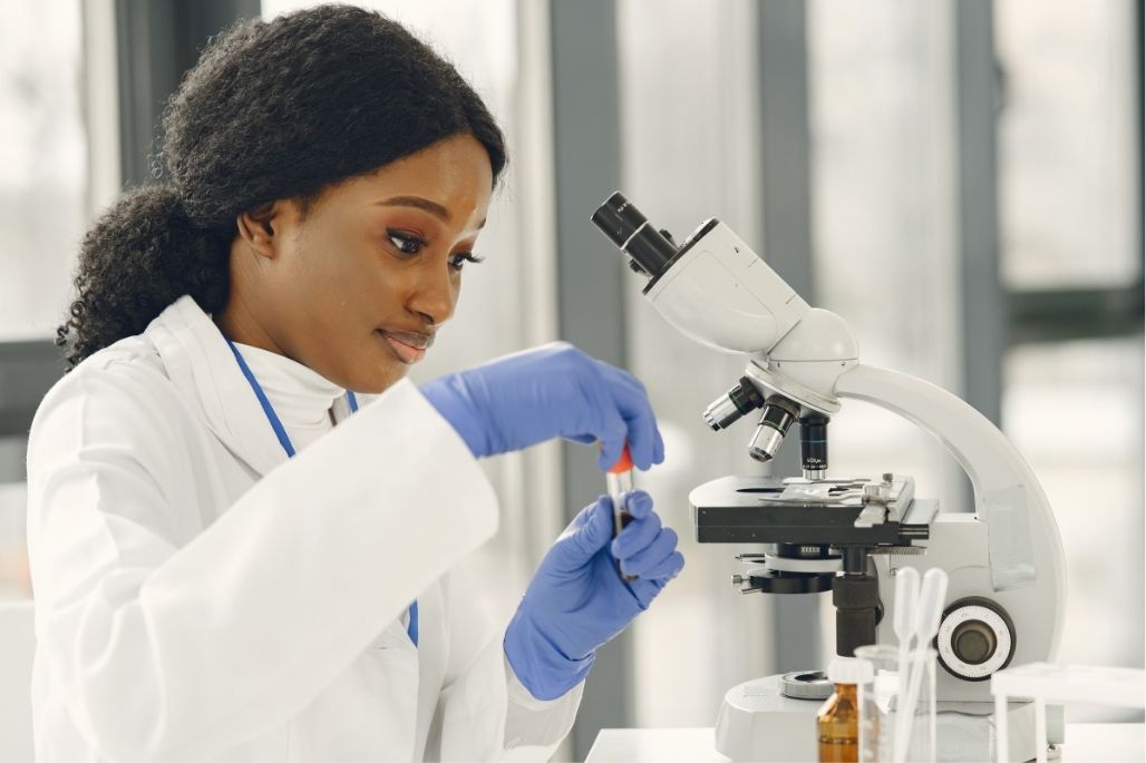 Medical laboratory assistant preparing a specimen slide beside a microscope in a lab.