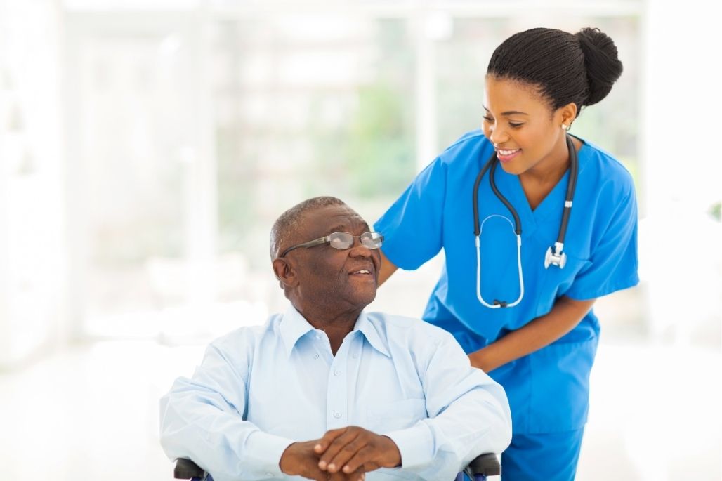 Patient care technician assisting a patient in a wheelchair in a healthcare setting.
