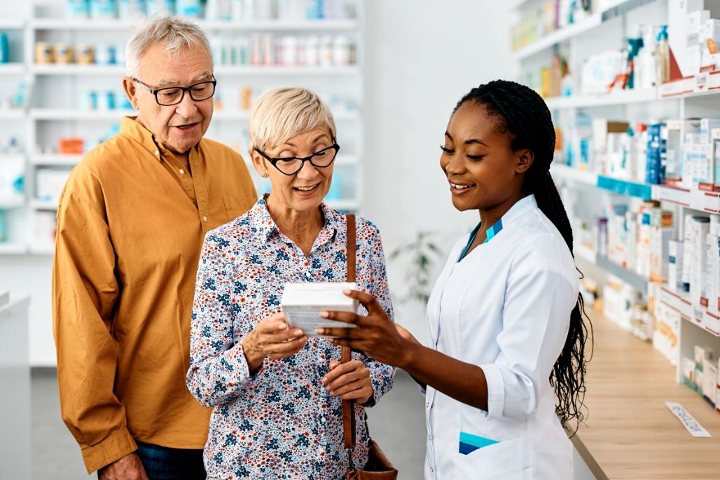 Pharmacy technician reviewing a prescription bottle with a patient in a pharmacy.